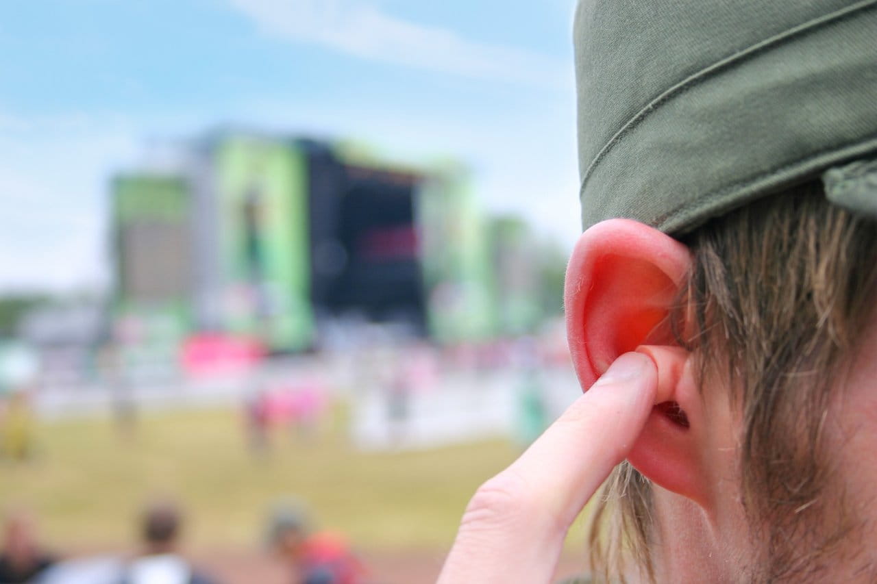 Man placing an earplug in his ear at an outdoor concert.