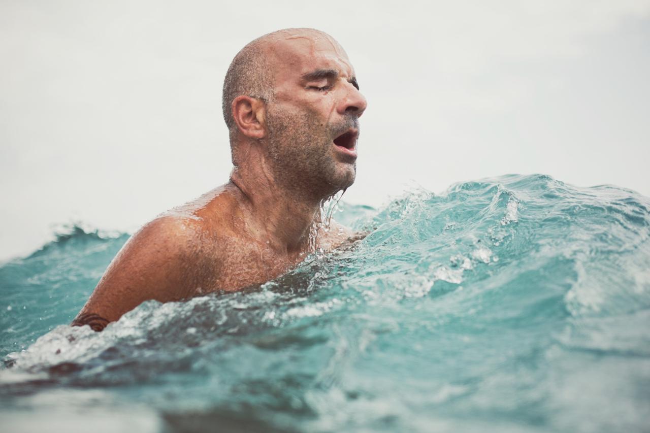Man swimming in open water with eyes closed, water splashing around.