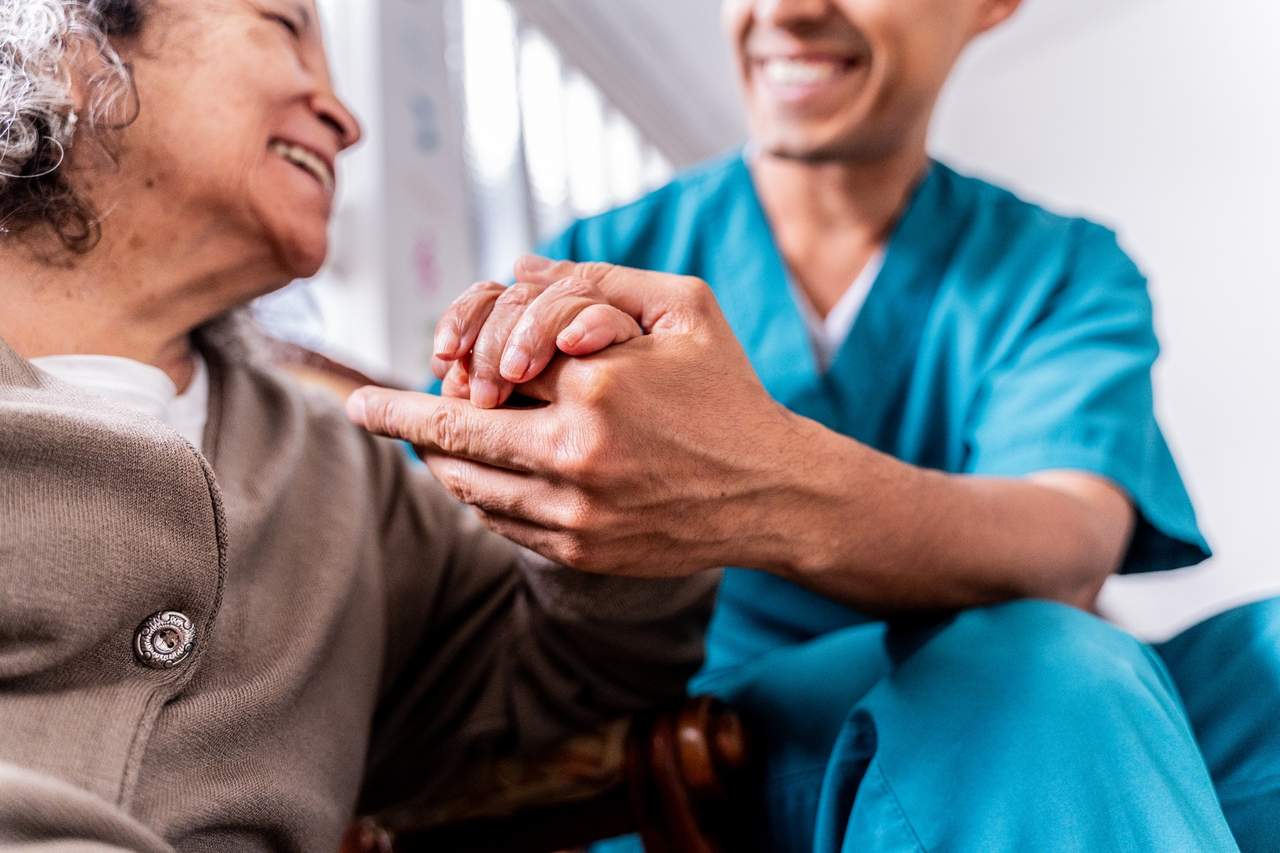 A healthcare worker in scrubs holding the hand of an elderly woman