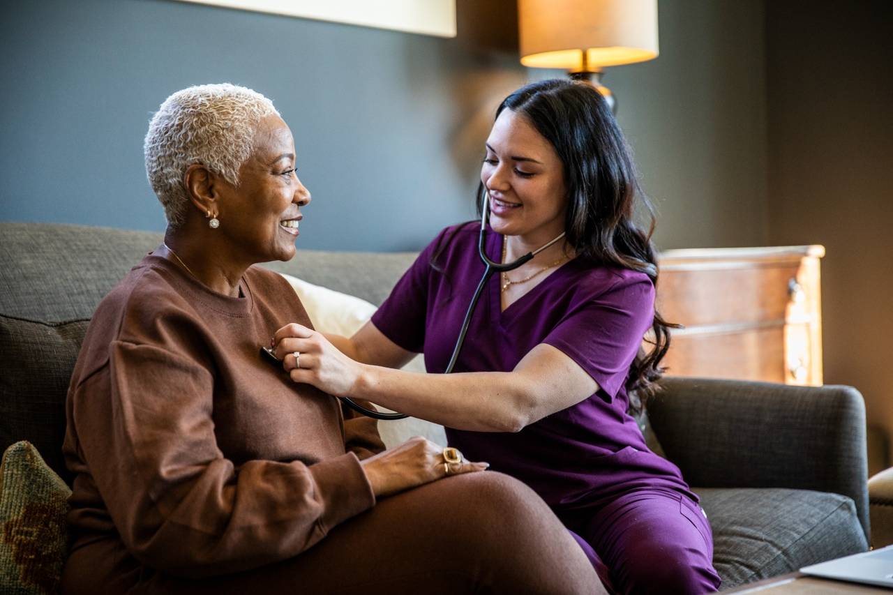 Home healthcare nurse checking patient’s heart with a stethoscope