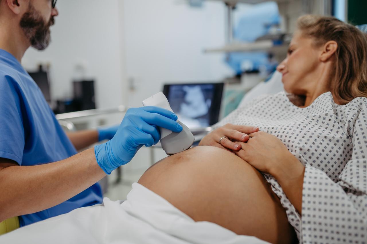 Technician performs ultrasound scan on pregnant belly.