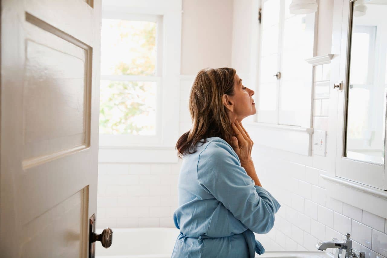 Woman touching her neck by the mirror