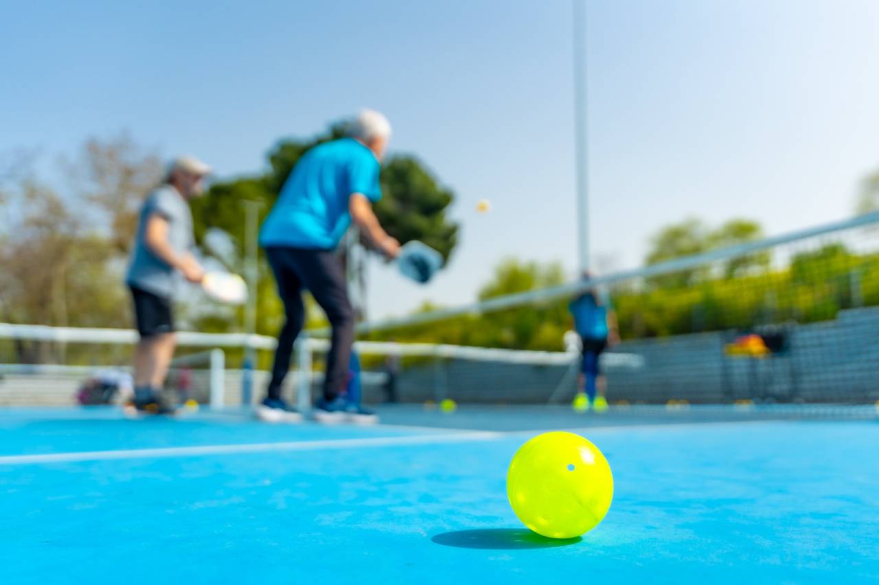 Yellow pickleball ball on blue court with players in background