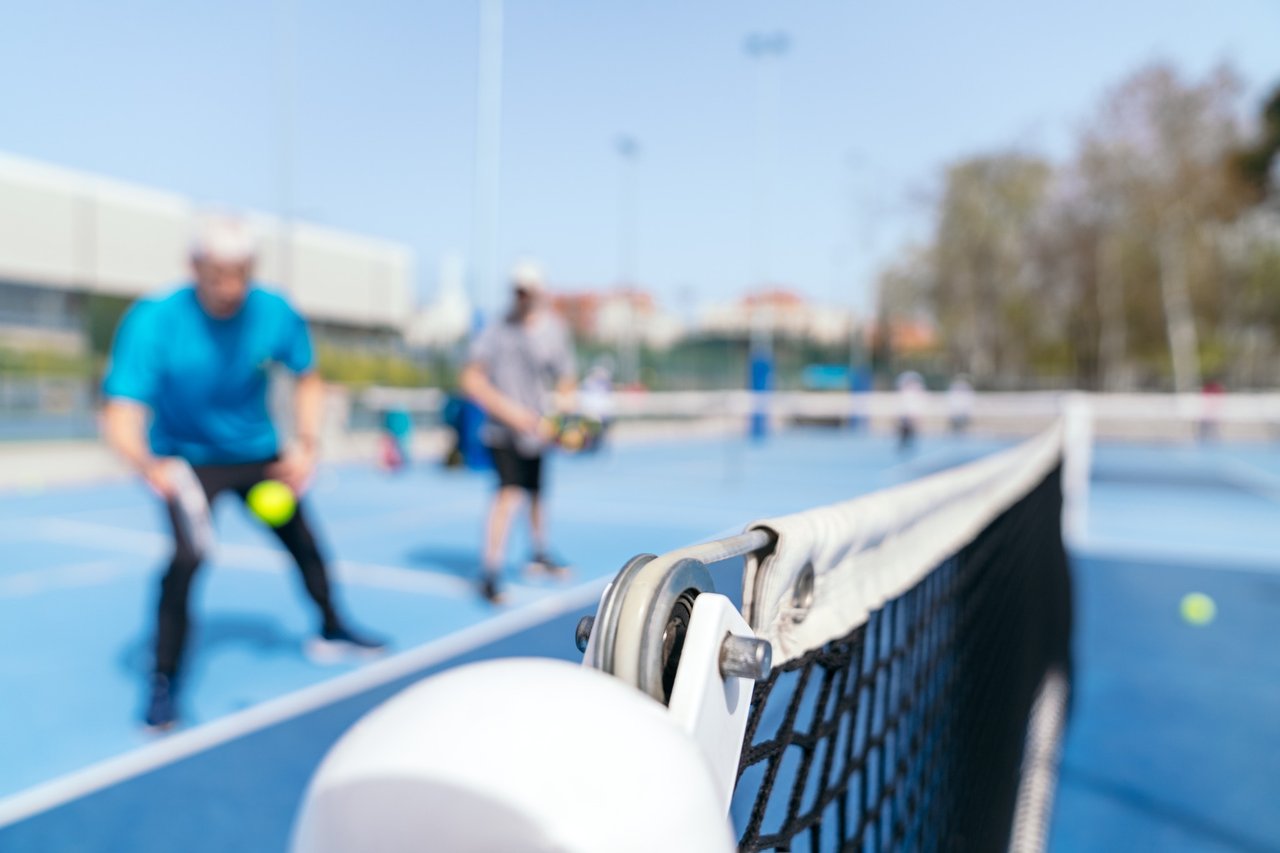 Pickleball net close-up with players in background. 