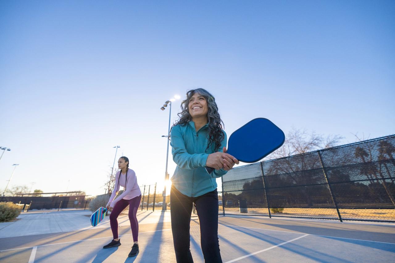 Two women playing pickleball outdoors at sunset