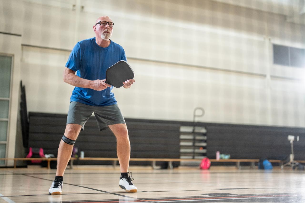 Older man with knee band playing pickleball