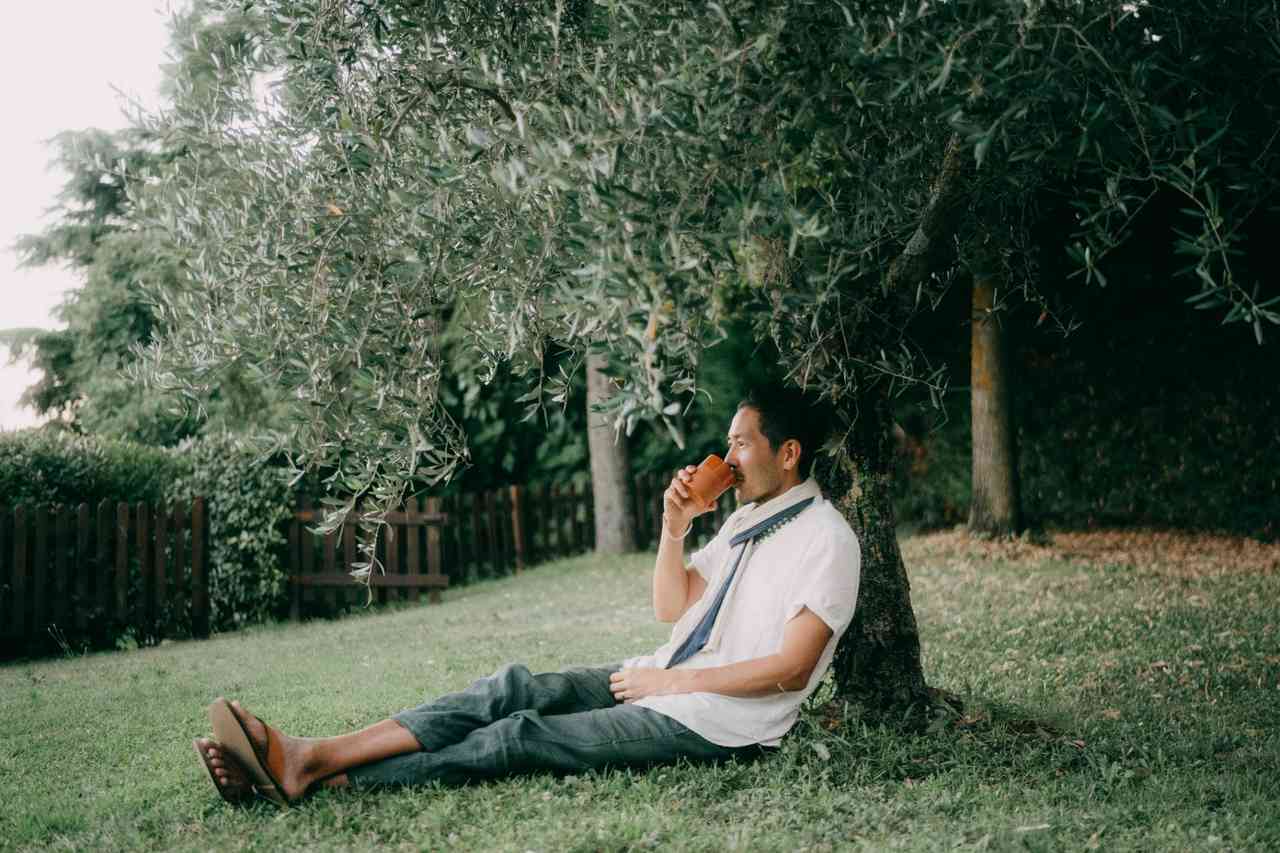 Man sipping drink under shady tree.
