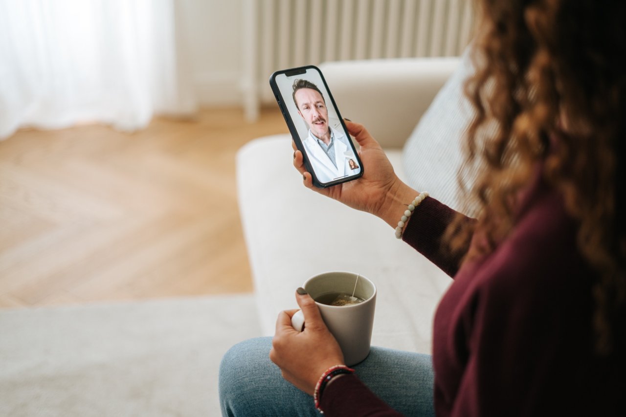 Woman having a virtual doctor visit on her smartphone while holding a cup of tea