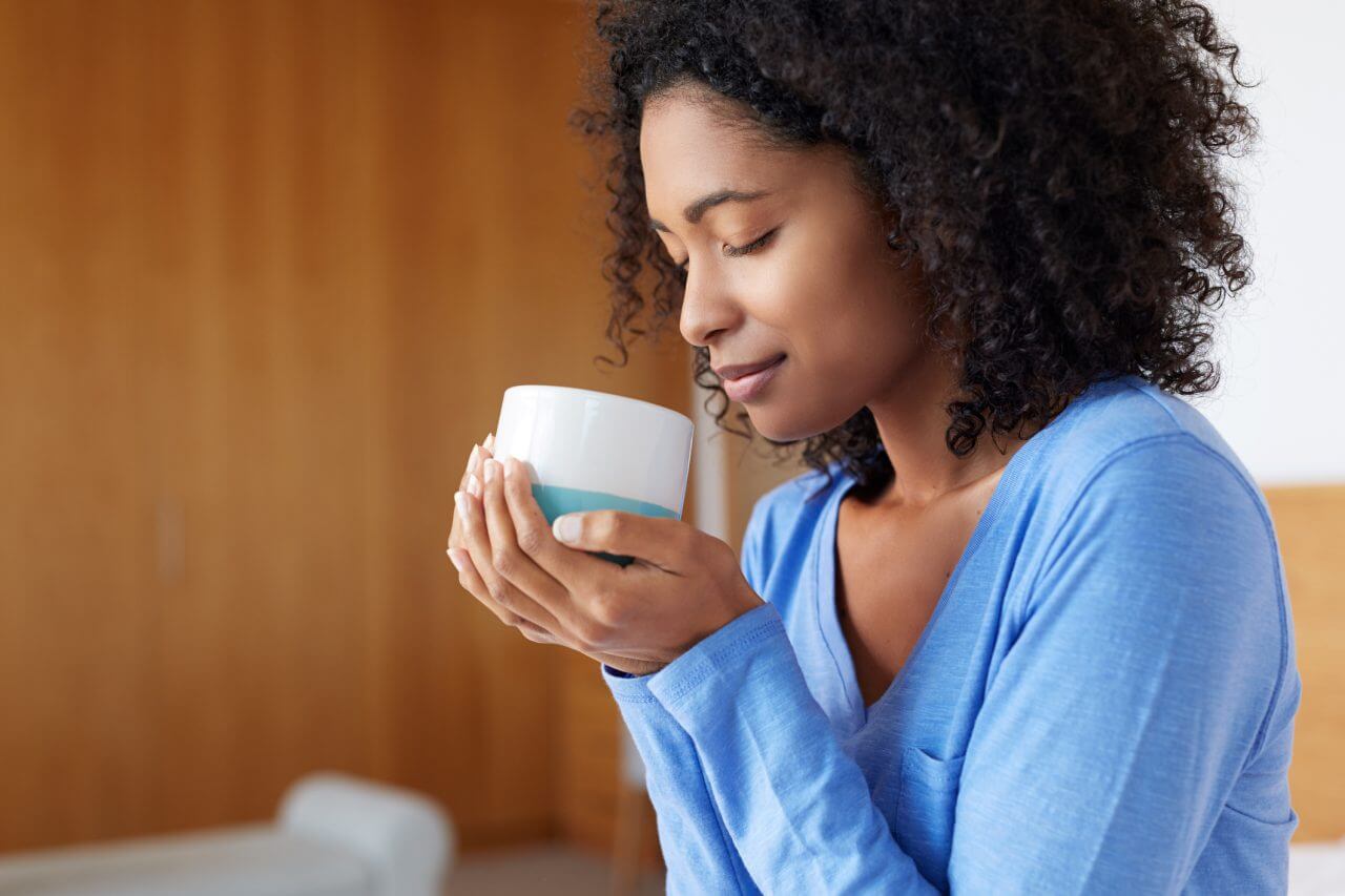 woman holding cup smiling with eyes closed
